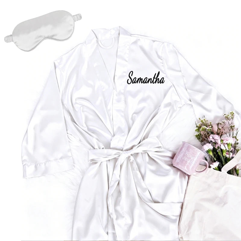 Personalized soft satin bridesmaid robe in custom pink with matching eye mask, shown on bachelorette gift display.