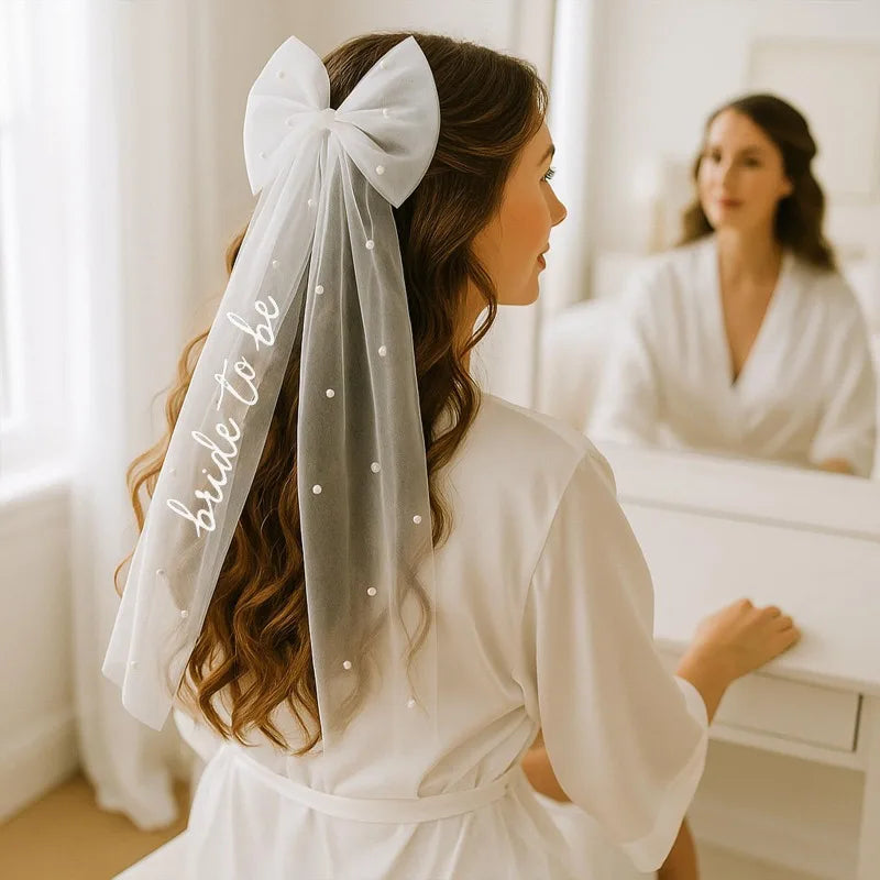 White pearl hair bow clip with attached tulle veil, shown on bride-to-be bachelorette accessory display.