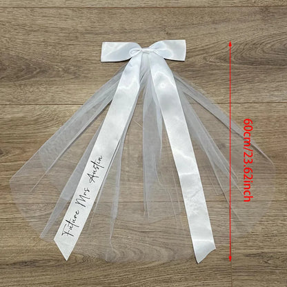 Personalized 'Future Mrs' bow veil in white tulle with satin bow, shown on bachelorette bride accessory display.