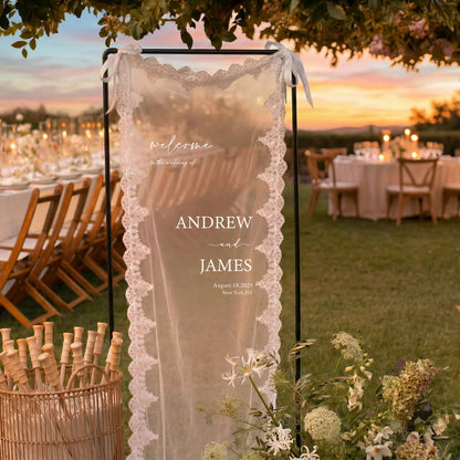 Personalized lace fabric wedding welcome banner with embroidered custom names and date, shown on outdoor ceremony display.