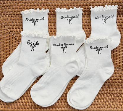 White wedding day socks with 'Bride Team' and 'Maid of Honor' lettering, shown on bridal party gift display.