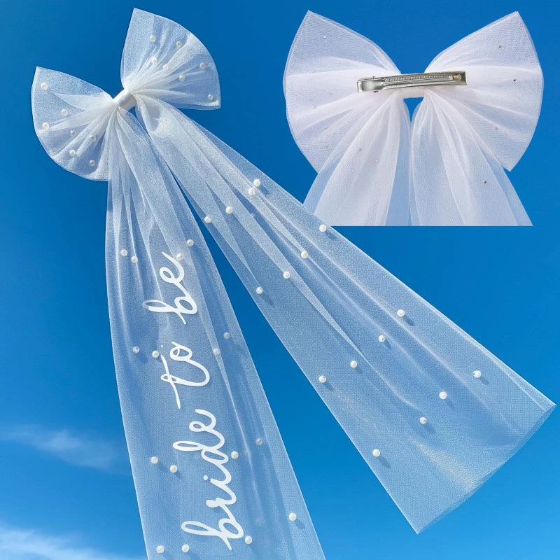 White pearl hair bow clip with attached tulle veil, shown on bride-to-be bachelorette accessory display.