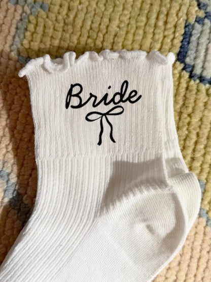 White wedding day socks with 'Bride Team' and 'Maid of Honor' lettering, shown on bridal party gift display.