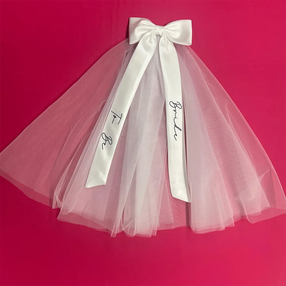 Bride to be pearl curvy veil in white tulle with satin bow, shown on bachelorette headpiece display.