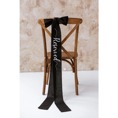 Elegant black 'Reserved' wedding chair seating ribbon, shown on ceremony chair display.