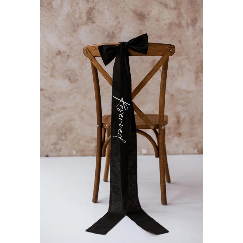 Elegant black 'Reserved' wedding chair seating ribbon, shown on ceremony chair display.