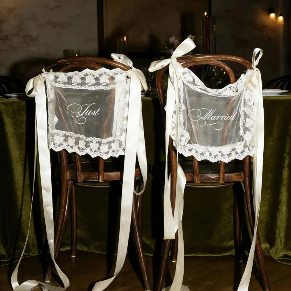 Sheer lace 'Just Married' chair sign set with 'Bride' and 'Groom' lettering, shown on wedding sweetheart table chair display.