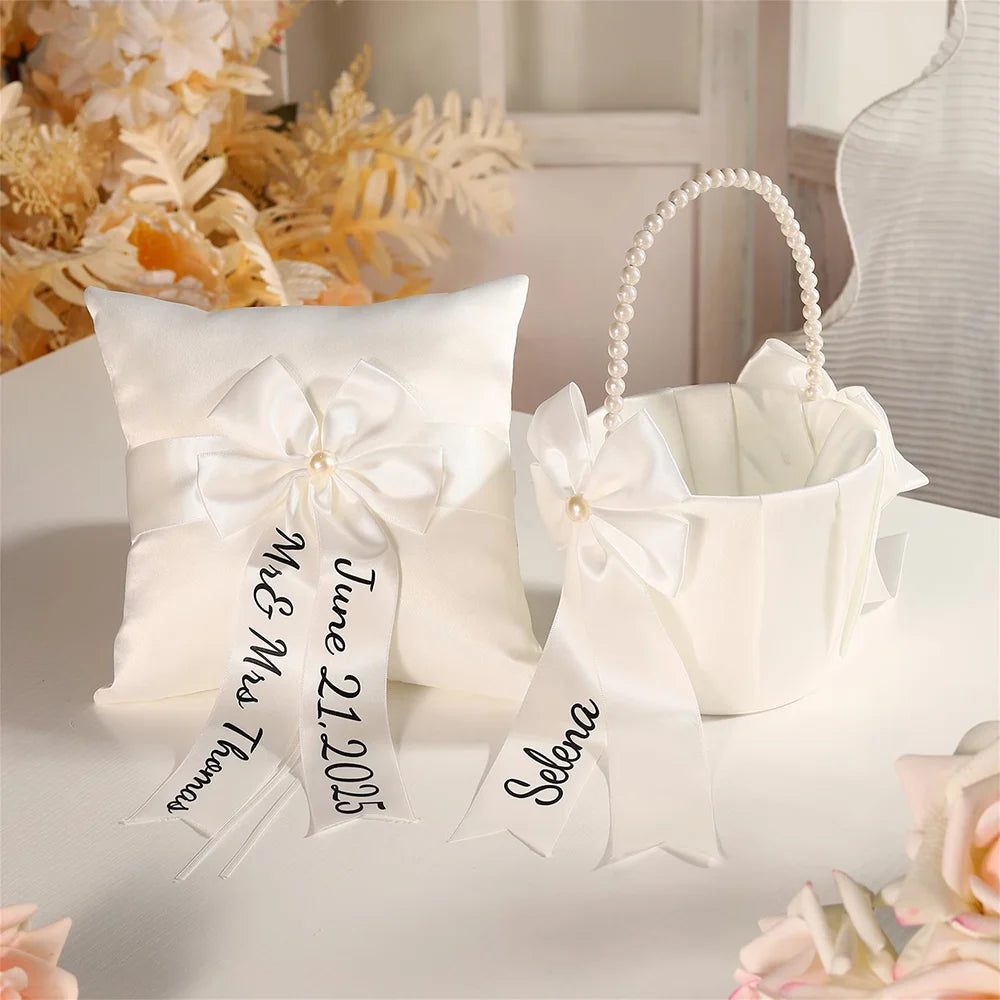 Personalized white flower girl basket and ring bearer pillow set with custom lettering, shown on wedding ceremony display.