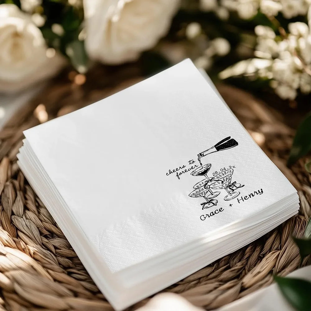 Custom 'Cheers To Forever' cocktail napkins personalized with names and wedding date, shown on champagne tower wedding reception display.