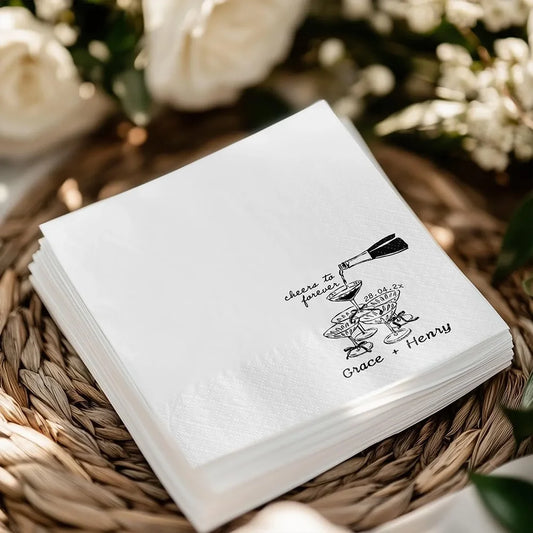 Custom 'Cheers To Forever' cocktail napkins personalized with names and wedding date, shown on champagne tower wedding reception display.