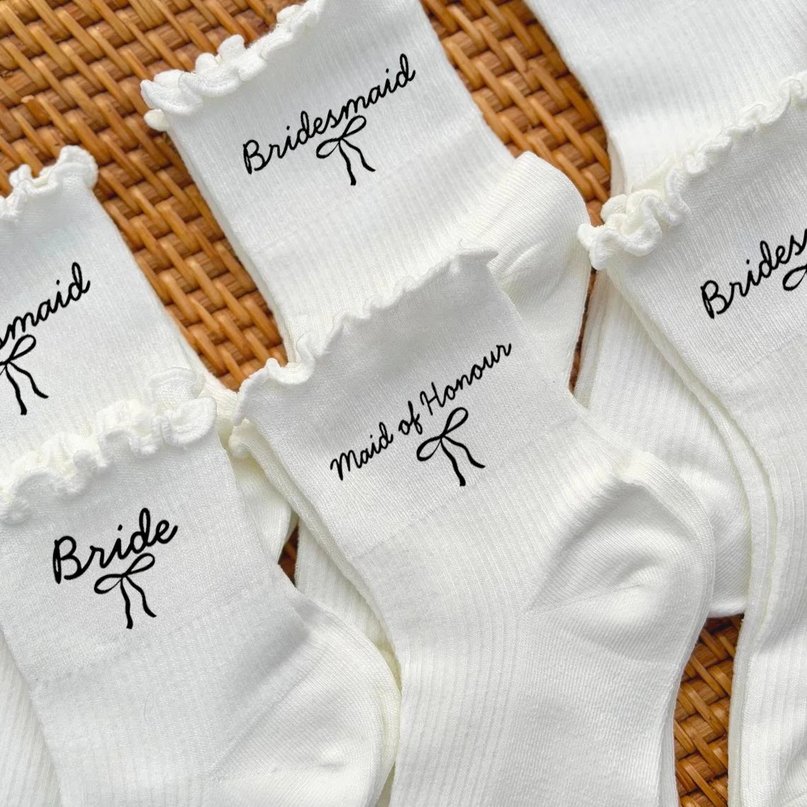 White wedding day socks with 'Bride Team' and 'Maid of Honor' lettering, shown on bridal party gift display.