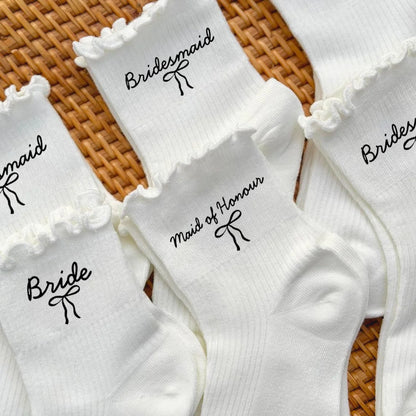White wedding day socks with 'Bride Team' and 'Maid of Honor' lettering, shown on bridal party gift display.