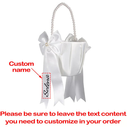 Personalized white flower girl basket and ring bearer pillow set with custom lettering, shown on wedding ceremony display.