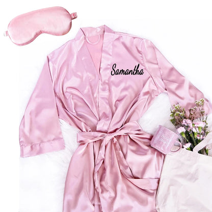 Personalized soft satin bridesmaid robe in custom pink with matching eye mask, shown on bachelorette gift display.