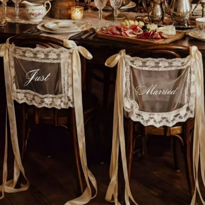Sheer lace 'Just Married' chair sign set with 'Bride' and 'Groom' lettering, shown on wedding sweetheart table chair display.