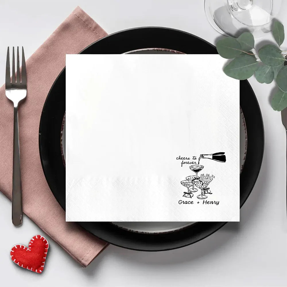 Custom 'Cheers To Forever' cocktail napkins personalized with names and wedding date, shown on champagne tower wedding reception display.