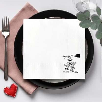Custom 'Cheers To Forever' cocktail napkins personalized with names and wedding date, shown on champagne tower wedding reception display.