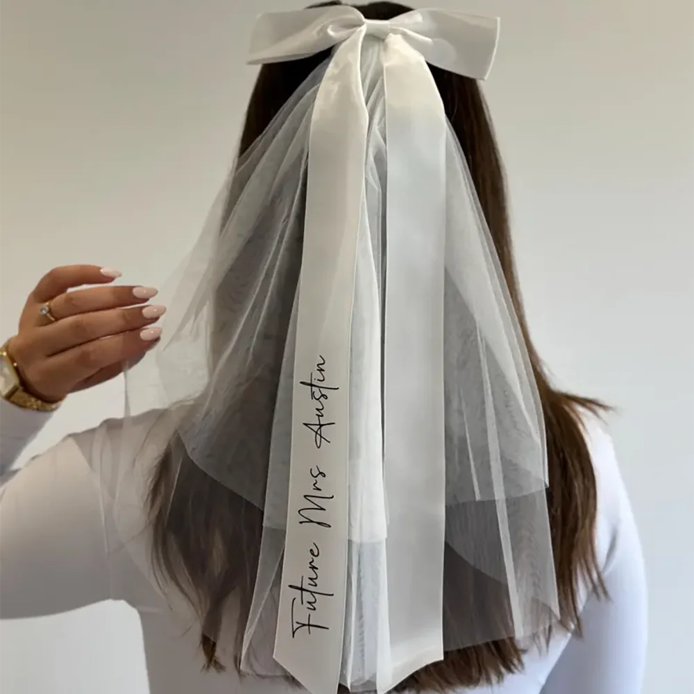 Personalized 'Future Mrs' bow veil in white tulle with satin bow, shown on bachelorette bride accessory display.