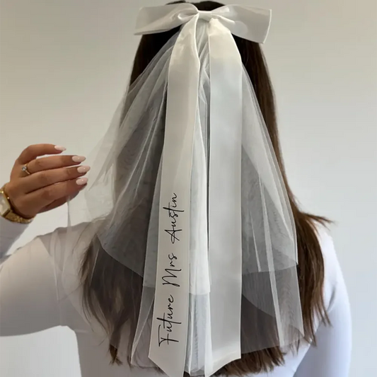 Personalized 'Future Mrs' bow veil in white tulle with satin bow, shown on bachelorette bride accessory display.