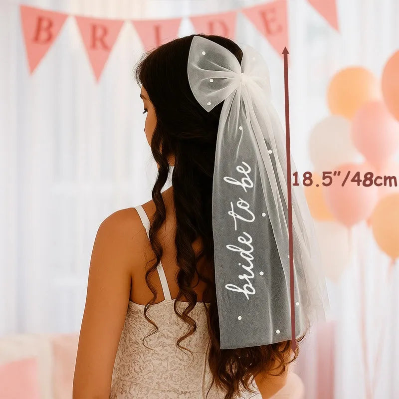 White pearl hair bow clip with attached tulle veil, shown on bride-to-be bachelorette accessory display.