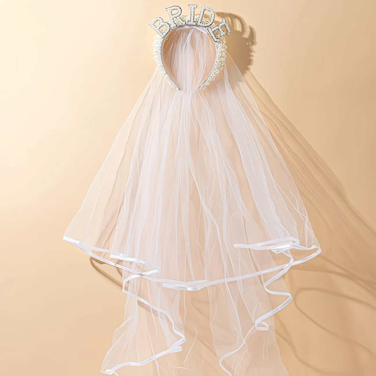 Bride to be pearl curvy veil in white tulle with satin bow, shown on bachelorette headpiece display.