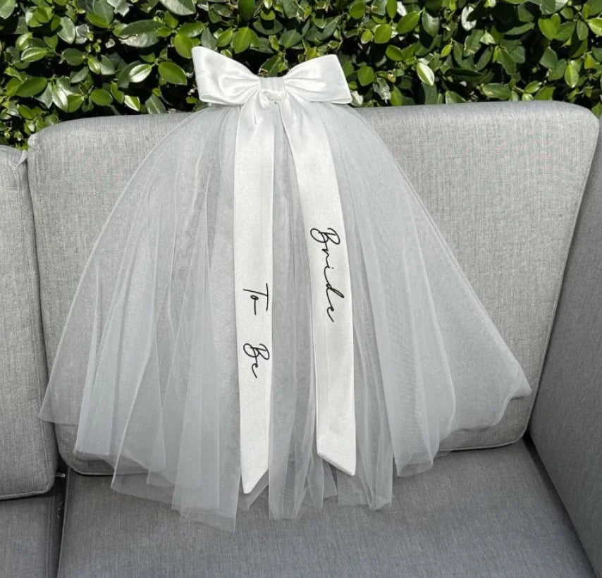 Bride to be pearl curvy veil in white tulle with satin bow, shown on bachelorette headpiece display.
