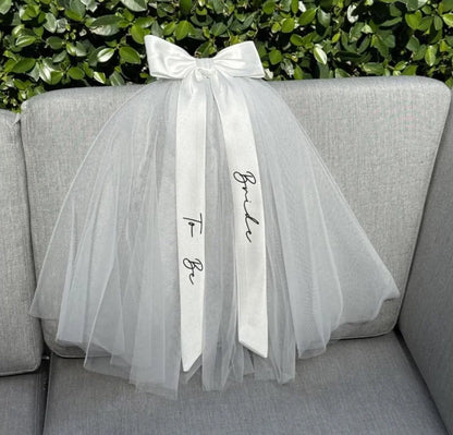 Bride to be pearl curvy veil in white tulle with satin bow, shown on bachelorette headpiece display.