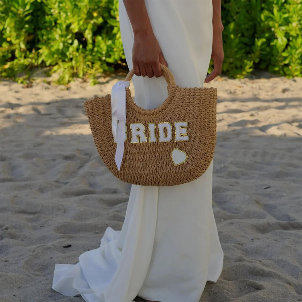 Bride straw tote beach bag with 'Bride' lettering, shown on bachelorette honeymoon accessory display.