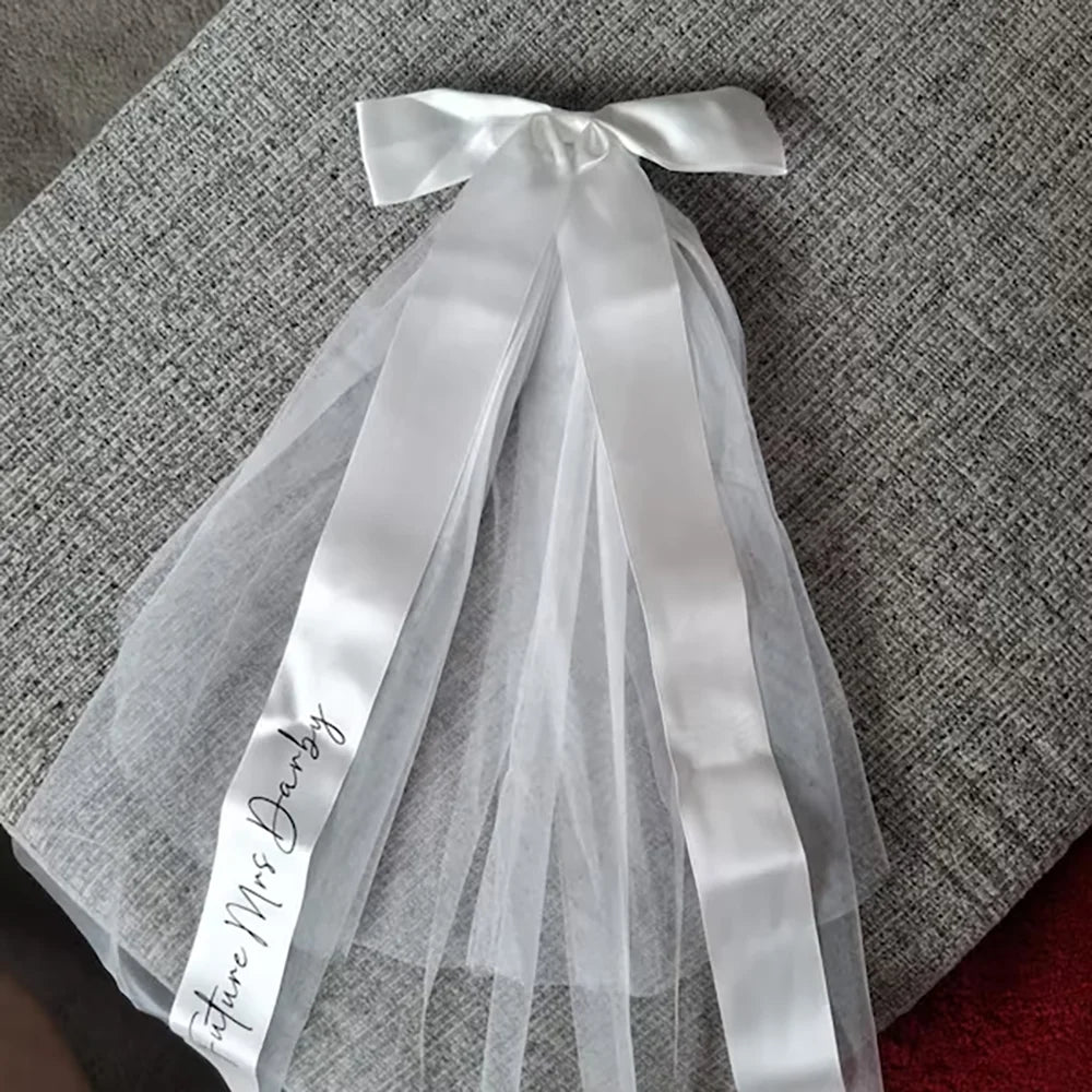 Personalized 'Future Mrs' bow veil in white tulle with satin bow, shown on bachelorette bride accessory display.